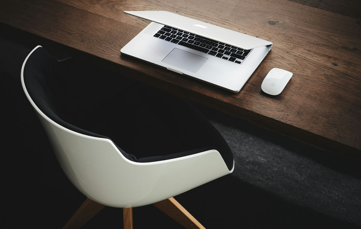 A partially open laptop on a dark wood table with an empty modern office chair 