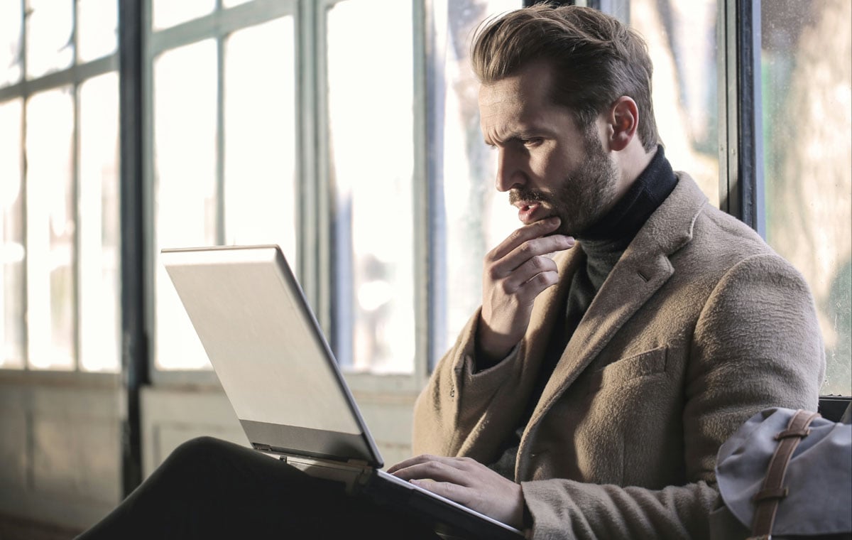 A businessman sits with a laptop near a window contemplating brand marketing vs performance marketing