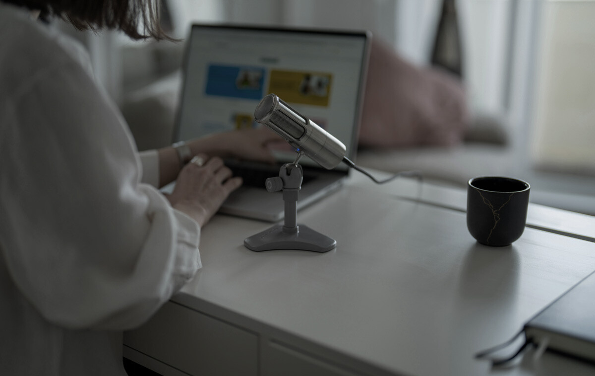 A woman sits at an open laptop with a microphone on the desk to show B2B content creation.