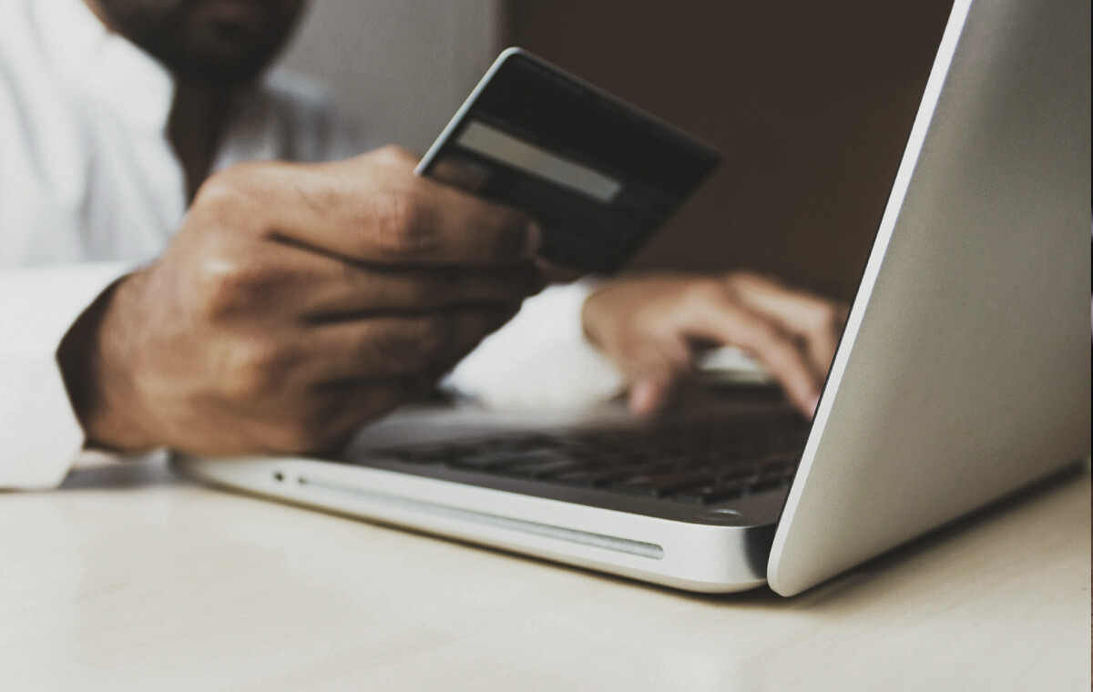 Close up image of a man holding a credit card and typing on a laptop, as though making a purchase to exemplify a b2b customer acquisition strategy