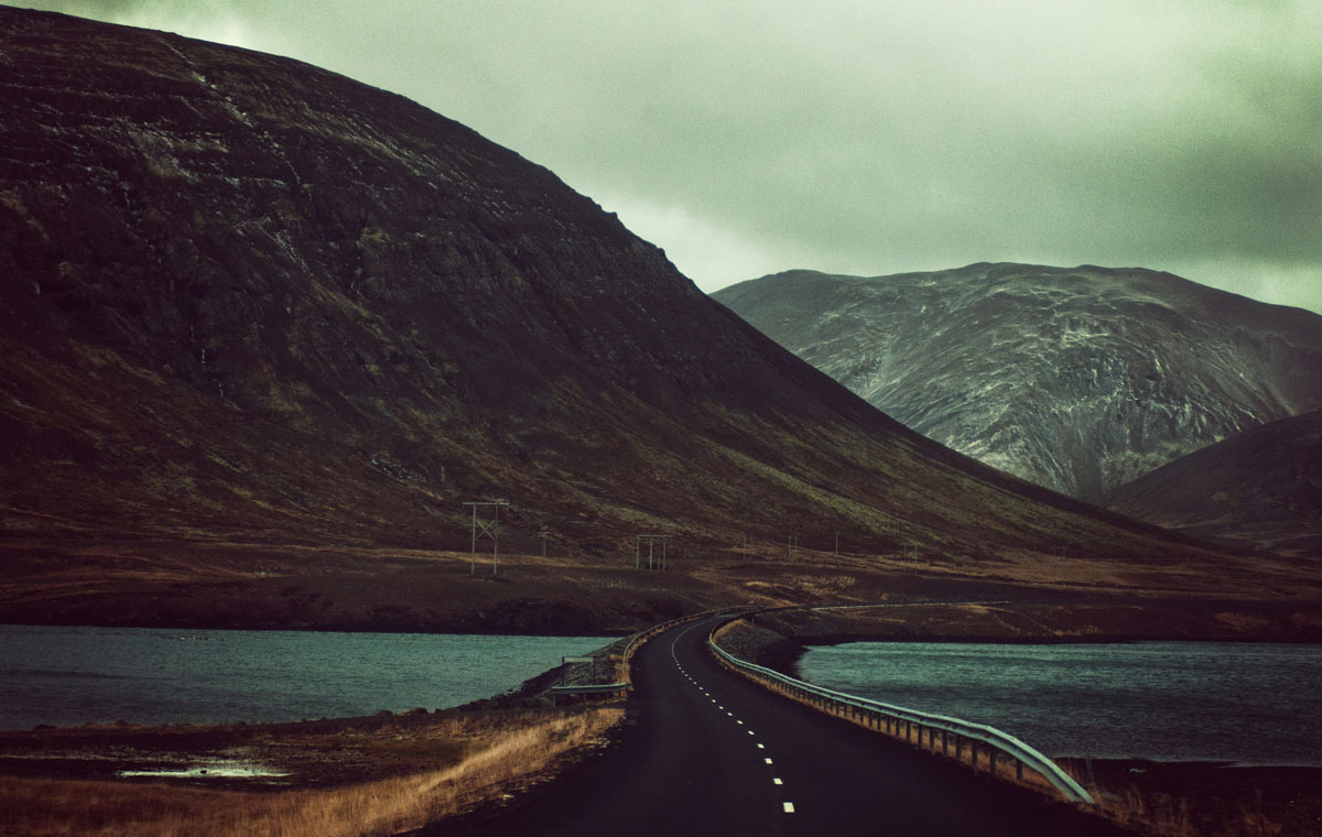 A scenic route with an empty road leading over a river towards mountains in the distance