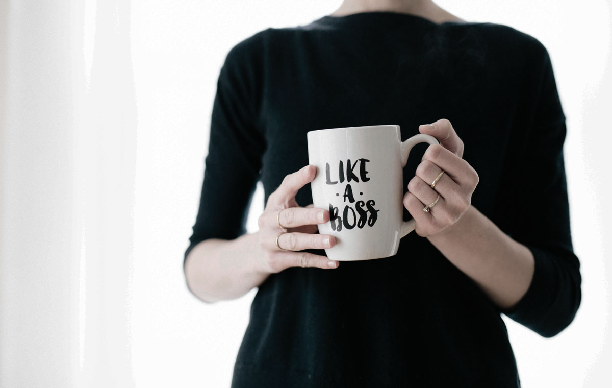 The torso of a woman in a black shirt holding a white mug that reads "like a boss."