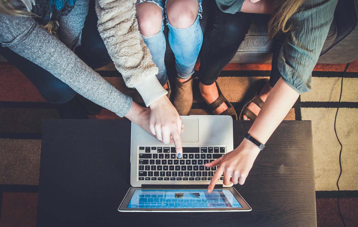 A group of people are gathered around a laptop collaborating on a multichannel marketing strategy