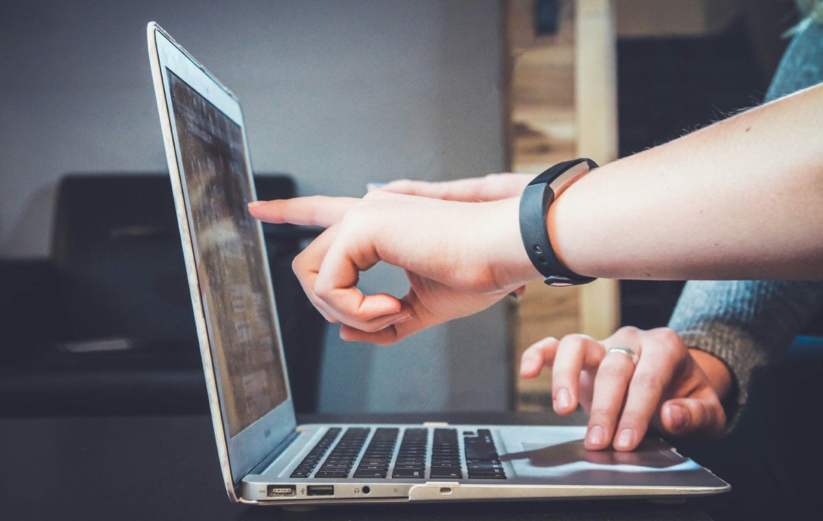 A woman wearing a watch points at a laptop screen 