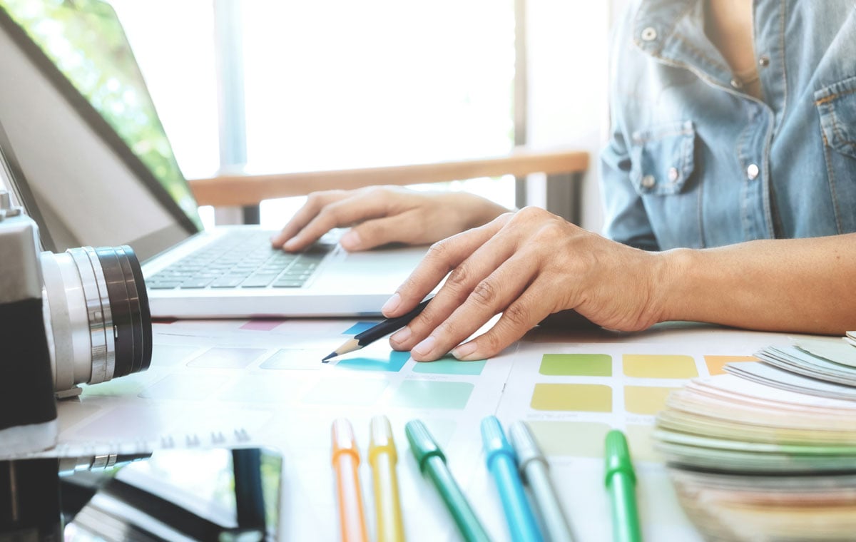 A woman works at a laptop on a brand refresh surrounded by designs and colorful markers